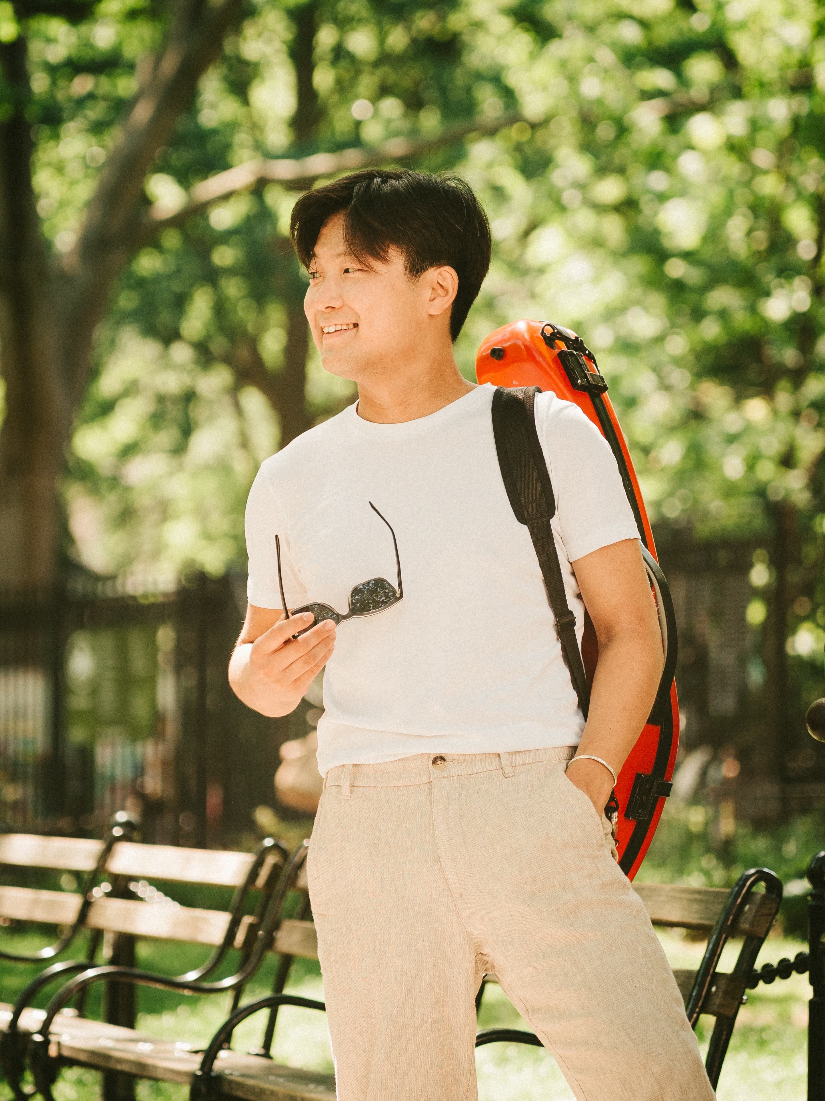 Siwoo Kim smiling in a park, his red violin case on his back