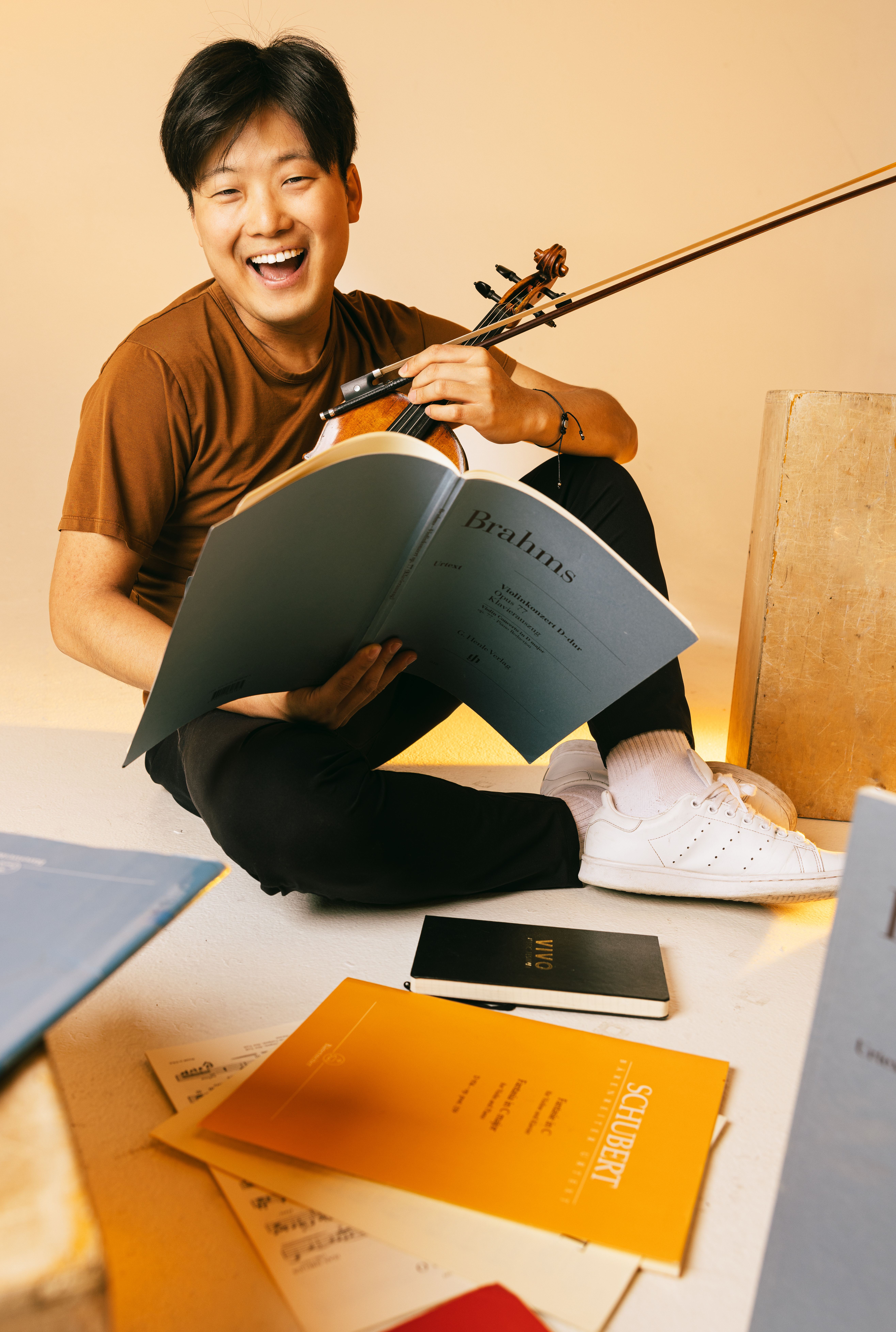 Siwoo Kim laughing on the floor with a score open in his hands and his violin beside him